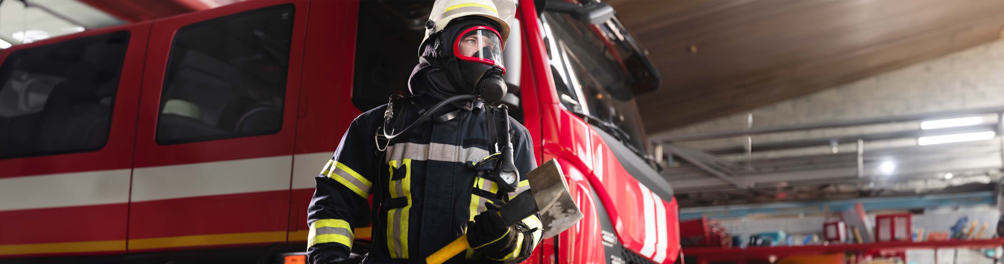 Professioneller Feuerwehrmann in voller Schutzausrüstung vor einem roten Feuerwehrfahrzeug, bereit für den Einsatz.