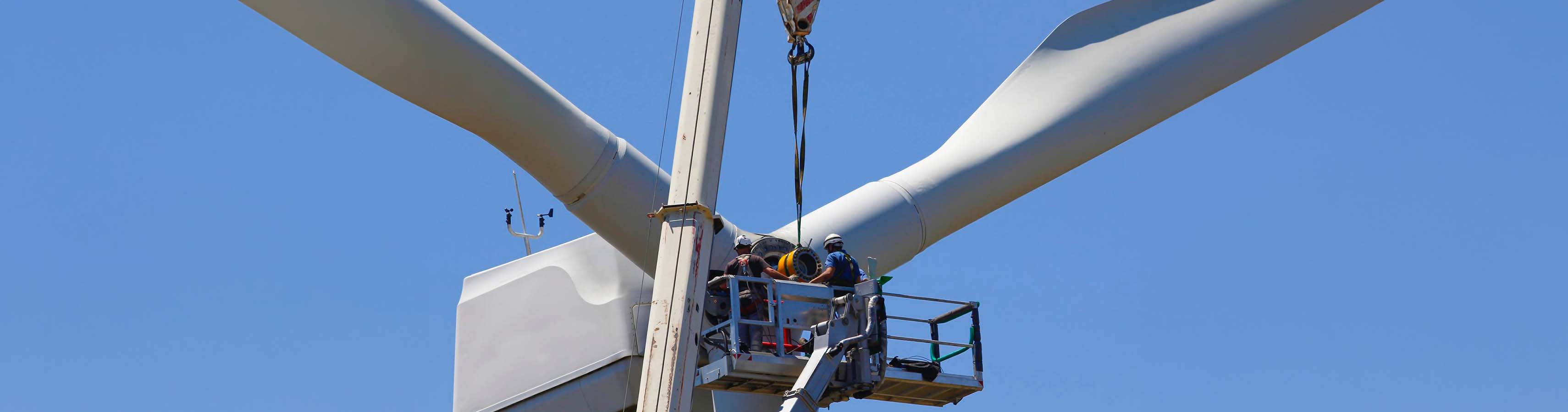 Techniker warten eine Windturbinennabe in schwindelerregender Höhe, gesichert durch Sicherheitsgurte und Helme