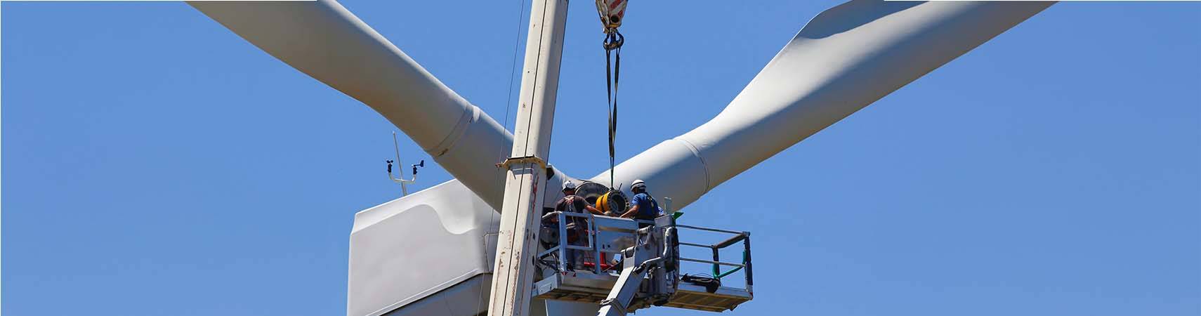 Techniker warten eine Windturbinennabe in schwindelerregender Höhe, gesichert durch Sicherheitsgurte und Helme